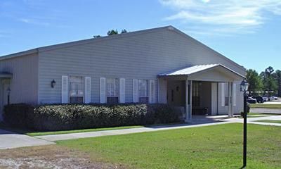 A low, light gray building with a white awning over the entrance and a row of windows.