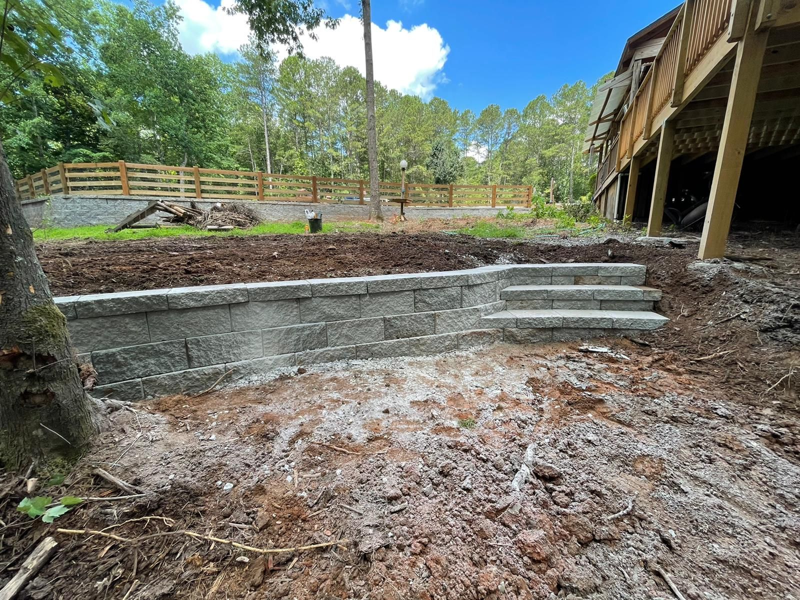 A stone wall and stairs are being built in the backyard of a house.