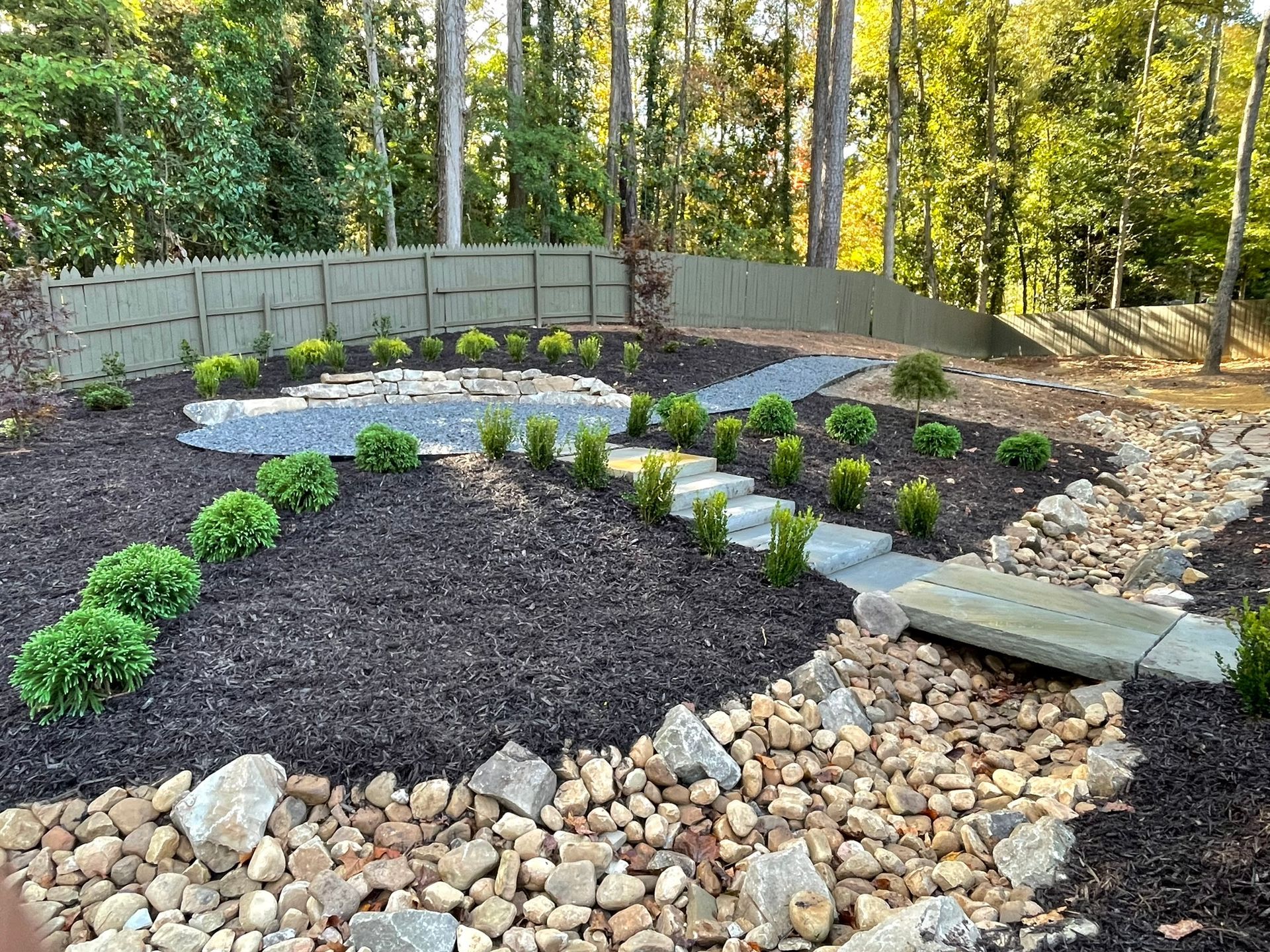 A backyard filled with rocks and plants with a fence in the background.