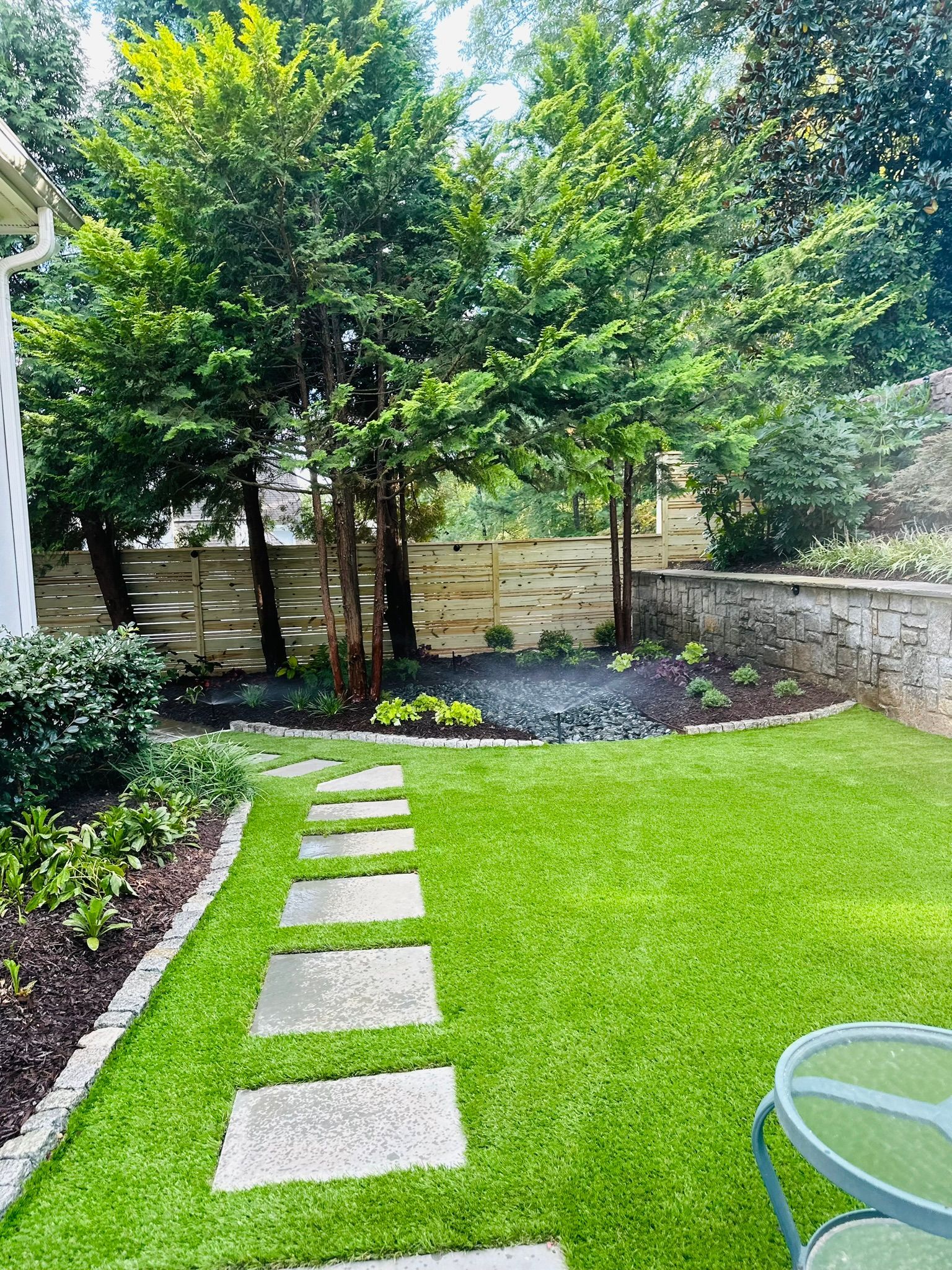 A backyard with a lush green lawn and a stone walkway.
