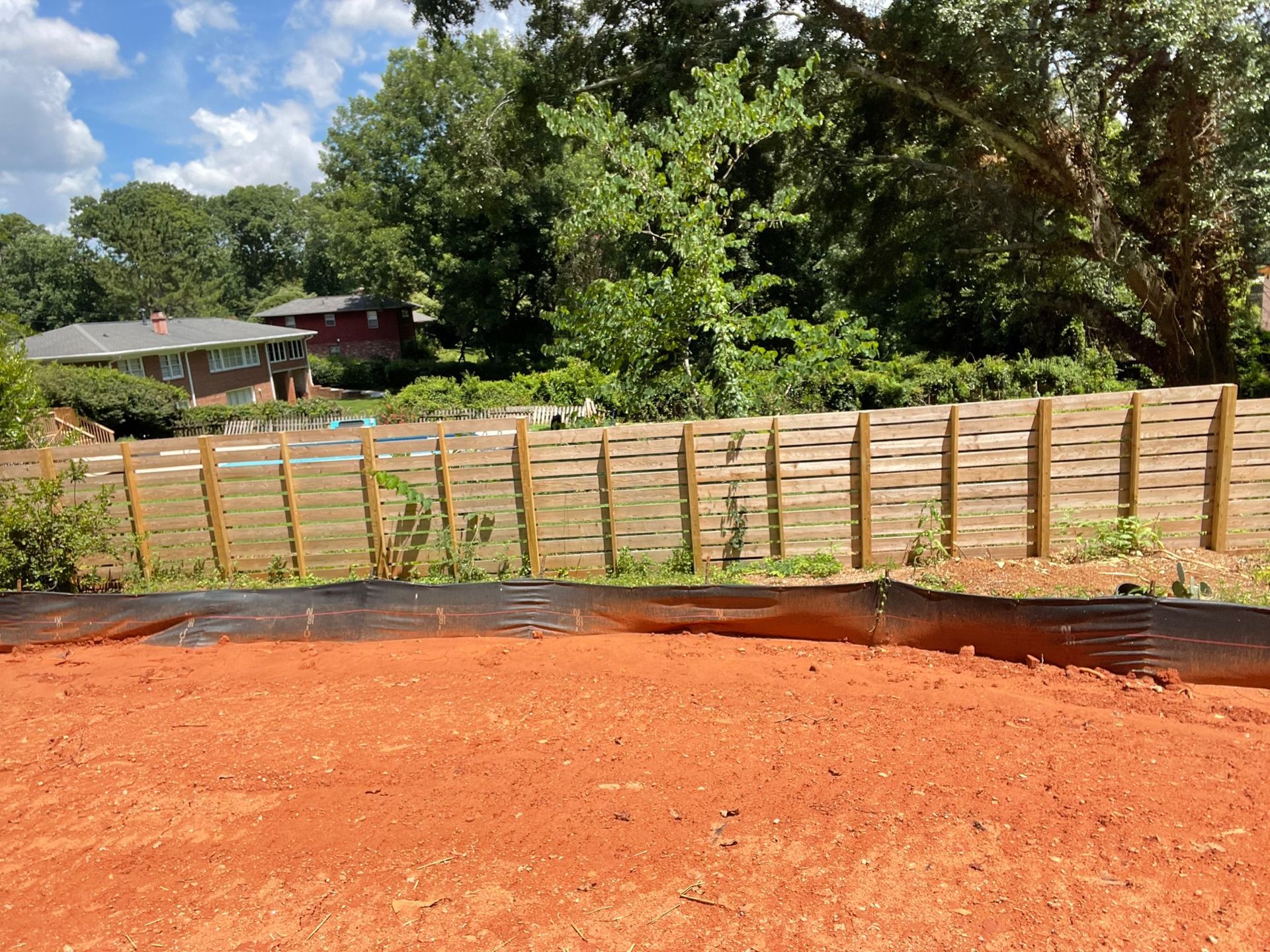 A wooden fence surrounds a dirt field in front of a house.