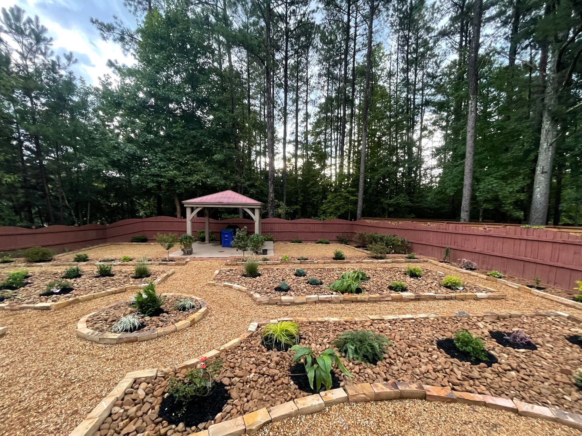 There is a gazebo in the middle of a garden surrounded by trees.