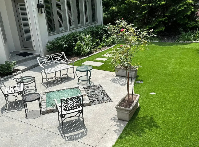 Modern backyard patio with artificial turf, potted plants, and wrought iron seating.