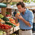 Man eating a cupcake at a farmers market beside crates of fresh fruits and vegetables