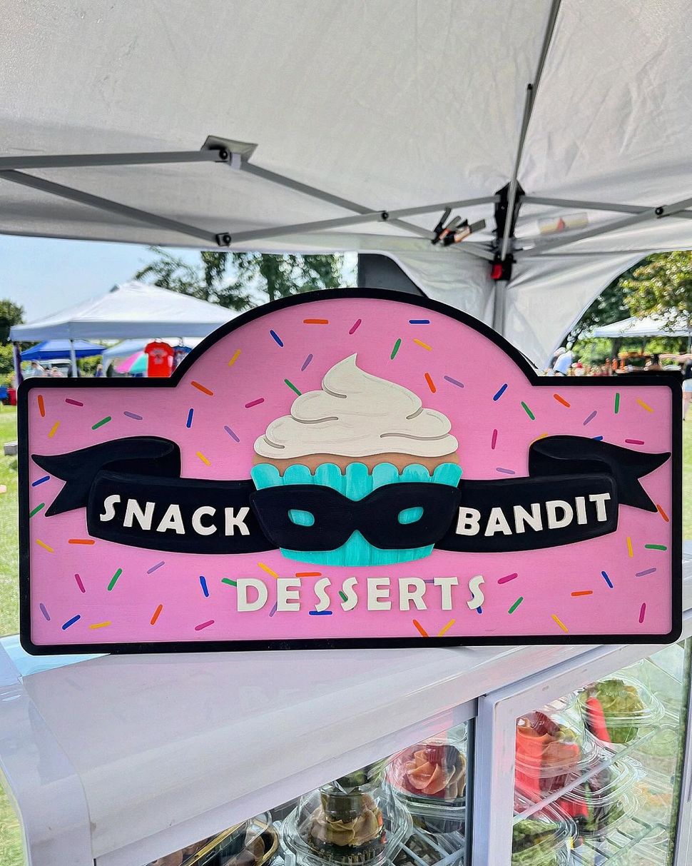 Pink dessert sign reading “Snack Bandit Desserts” under a white market tent.