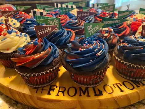 Assorted blue, red, and yellow frosted cupcakes on a wooden platter at a football-themed celebration