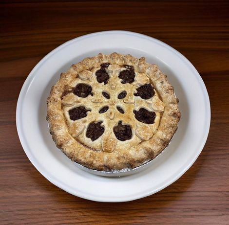 Golden pie with lattice crust and dark fruit filling on a white plate on a wooden table