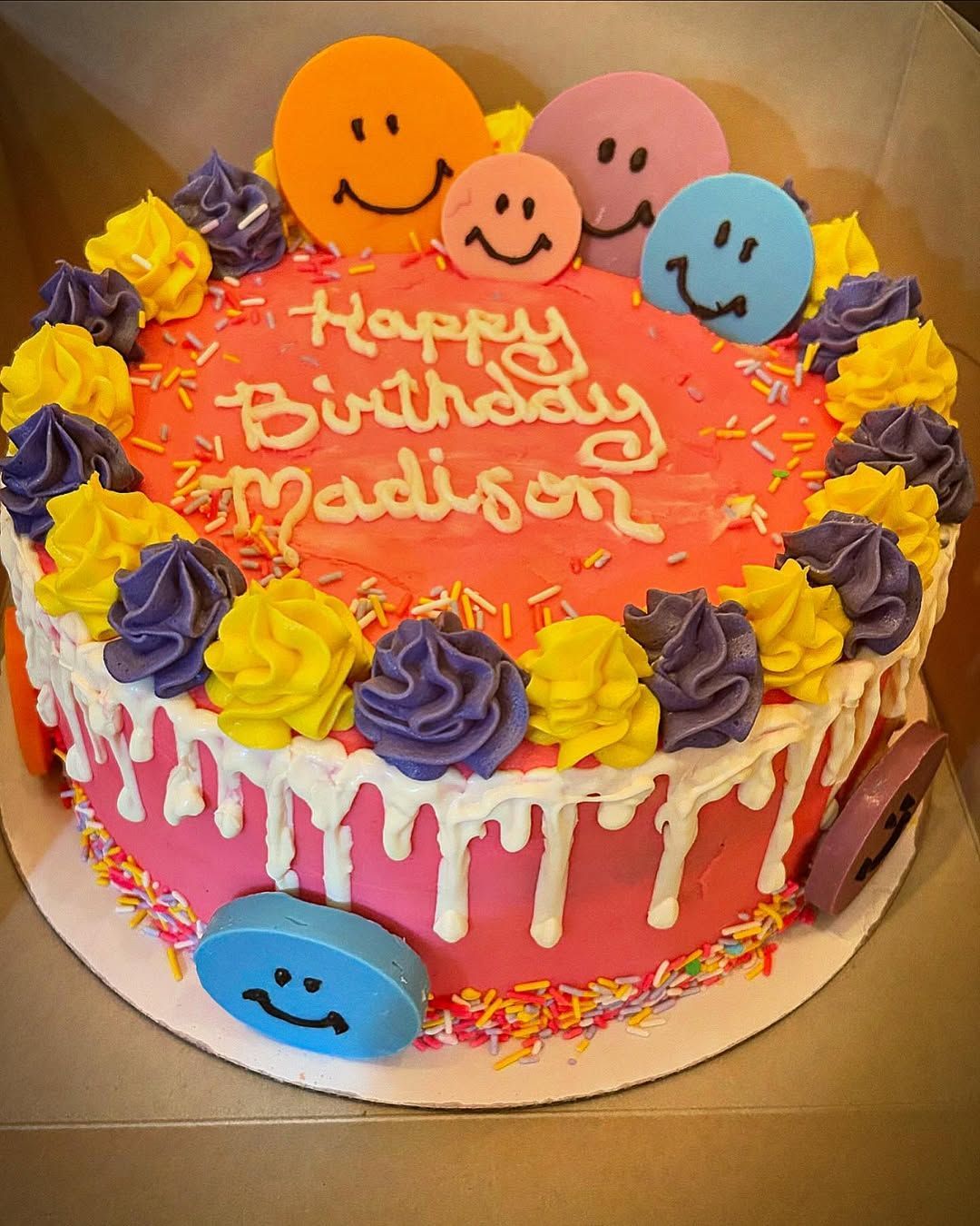 Birthday cake with pink frosting and colorful smiley face decorations, reading “Happy Birthday Madison.”