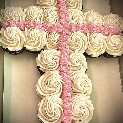 Cream-colored frosted cupcakes arranged in a cross on a cardboard tray with pink frosting lines