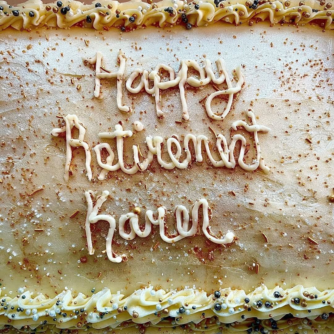 Frosted cake with piped icing reading “Happy Retirement Karen” on white icing.