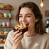 Woman smiling and taking a bite of a chocolate chip cookie in a cozy kitchen.