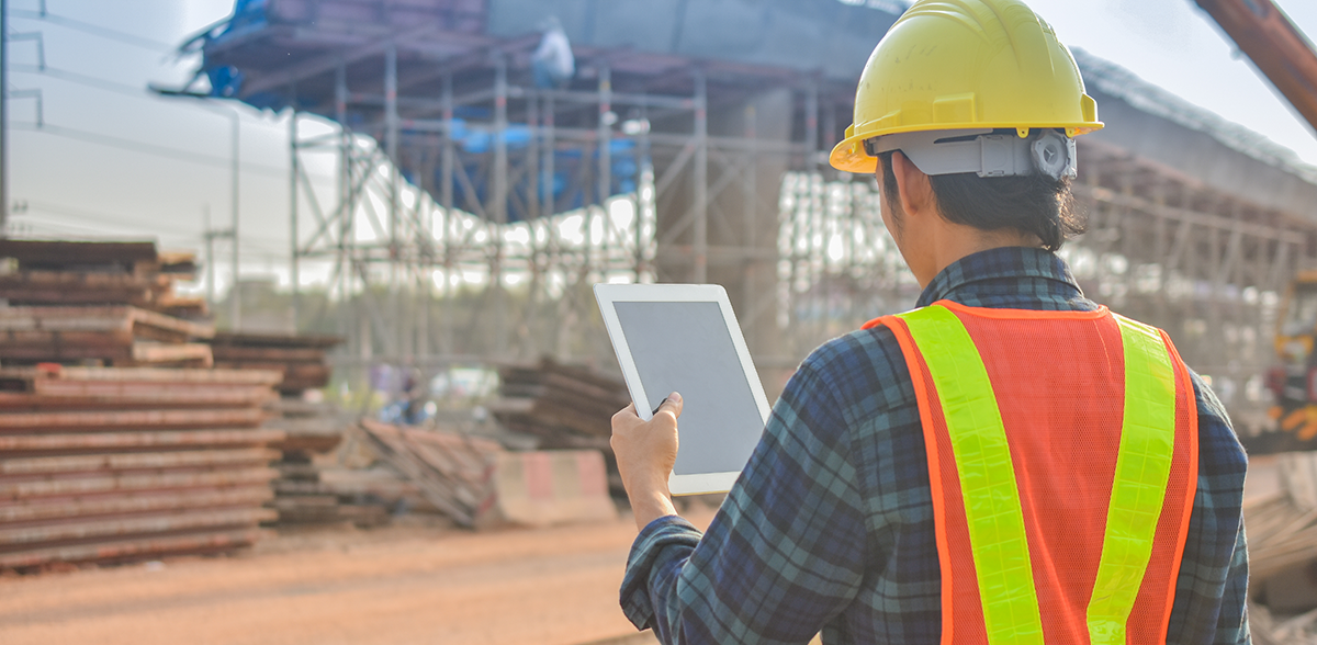 A construction worker is using a tablet computer at a construction site.