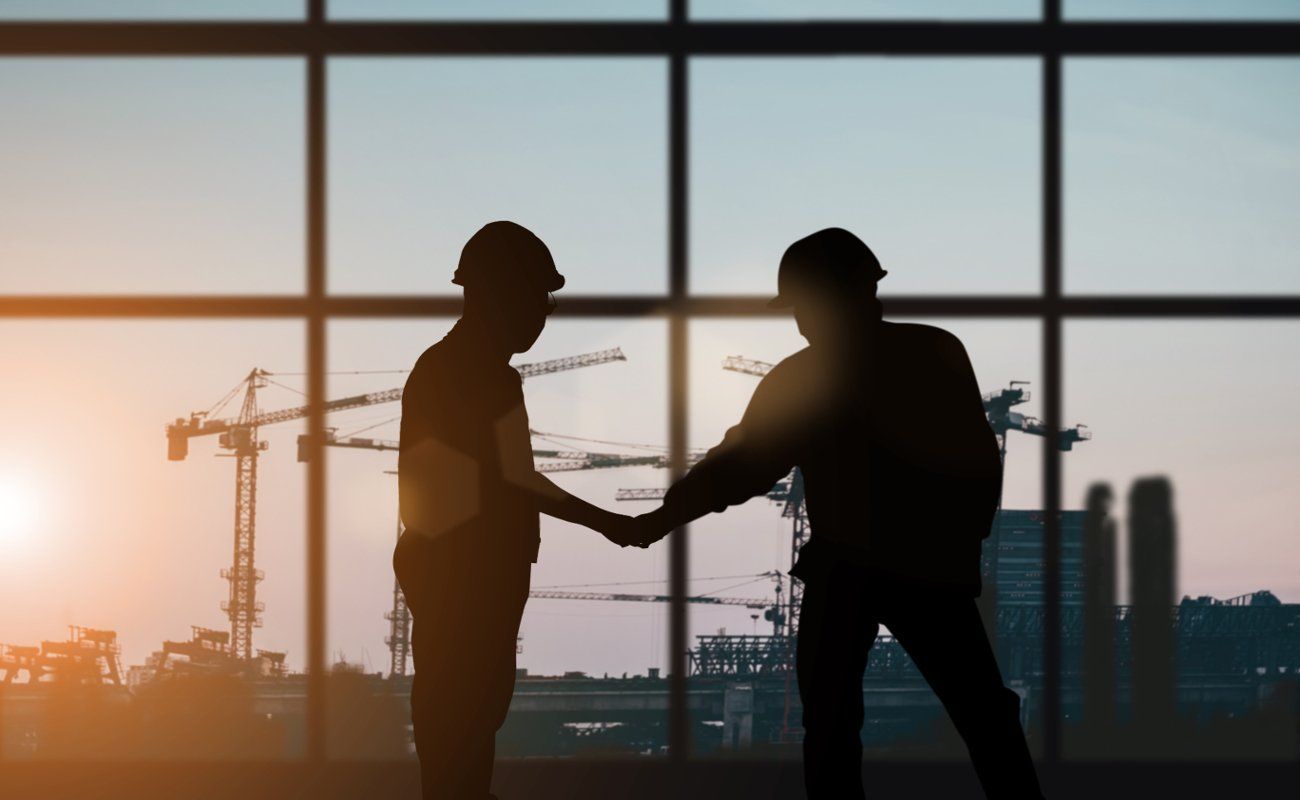 Two construction workers are shaking hands in front of a window.