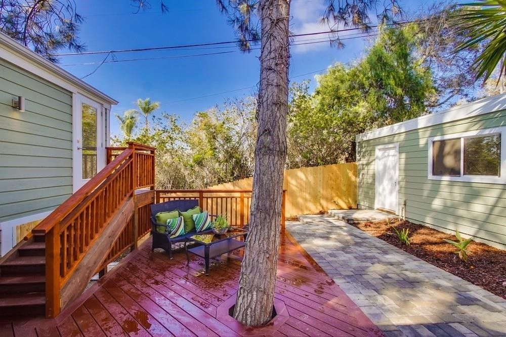 A backyard with a wooden deck , stairs , and a tree.
