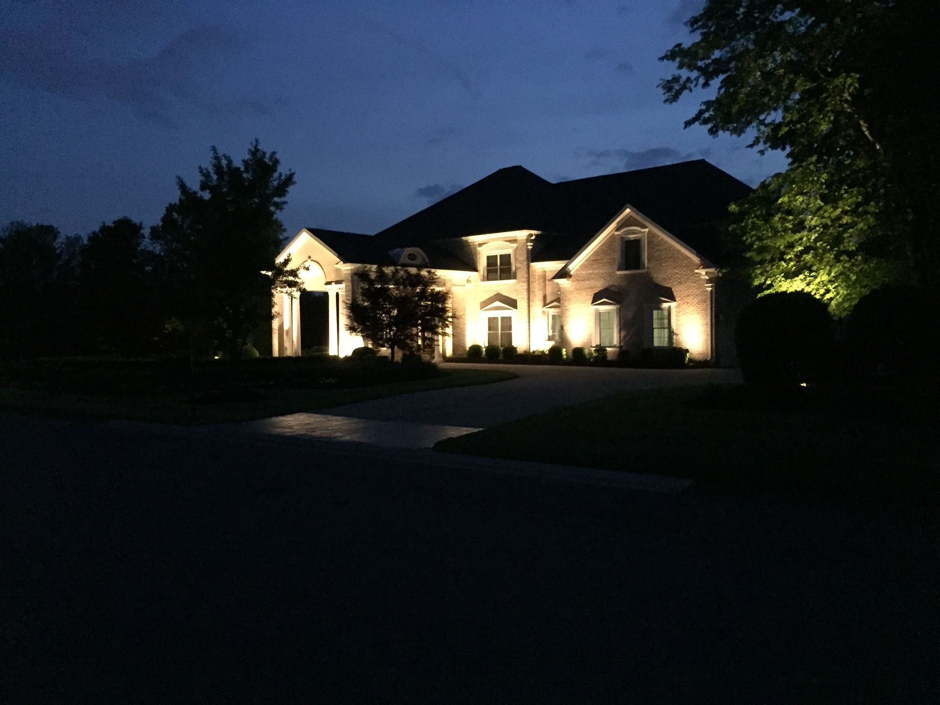 A two-story brick house at night, lit with spotlights, set against a dark blue sky.