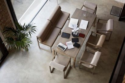 High-angle shot of a modern dining room with a long wooden table, chairs, and a bench. There are papers, notebooks, and a small plant on the table.