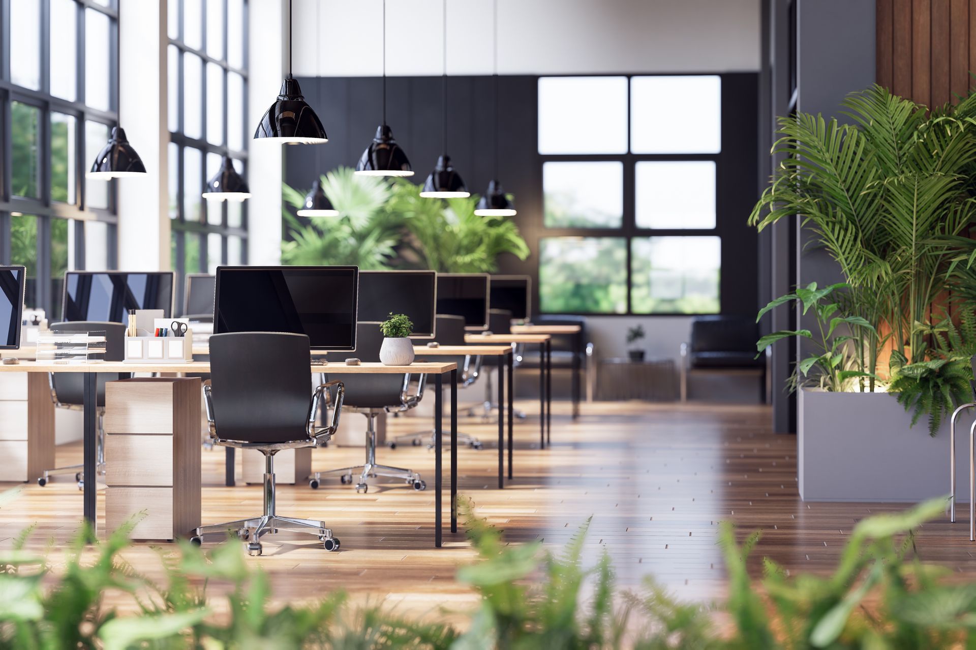 Modern office interior with desks, black chairs, and large windows overlooking greenery.