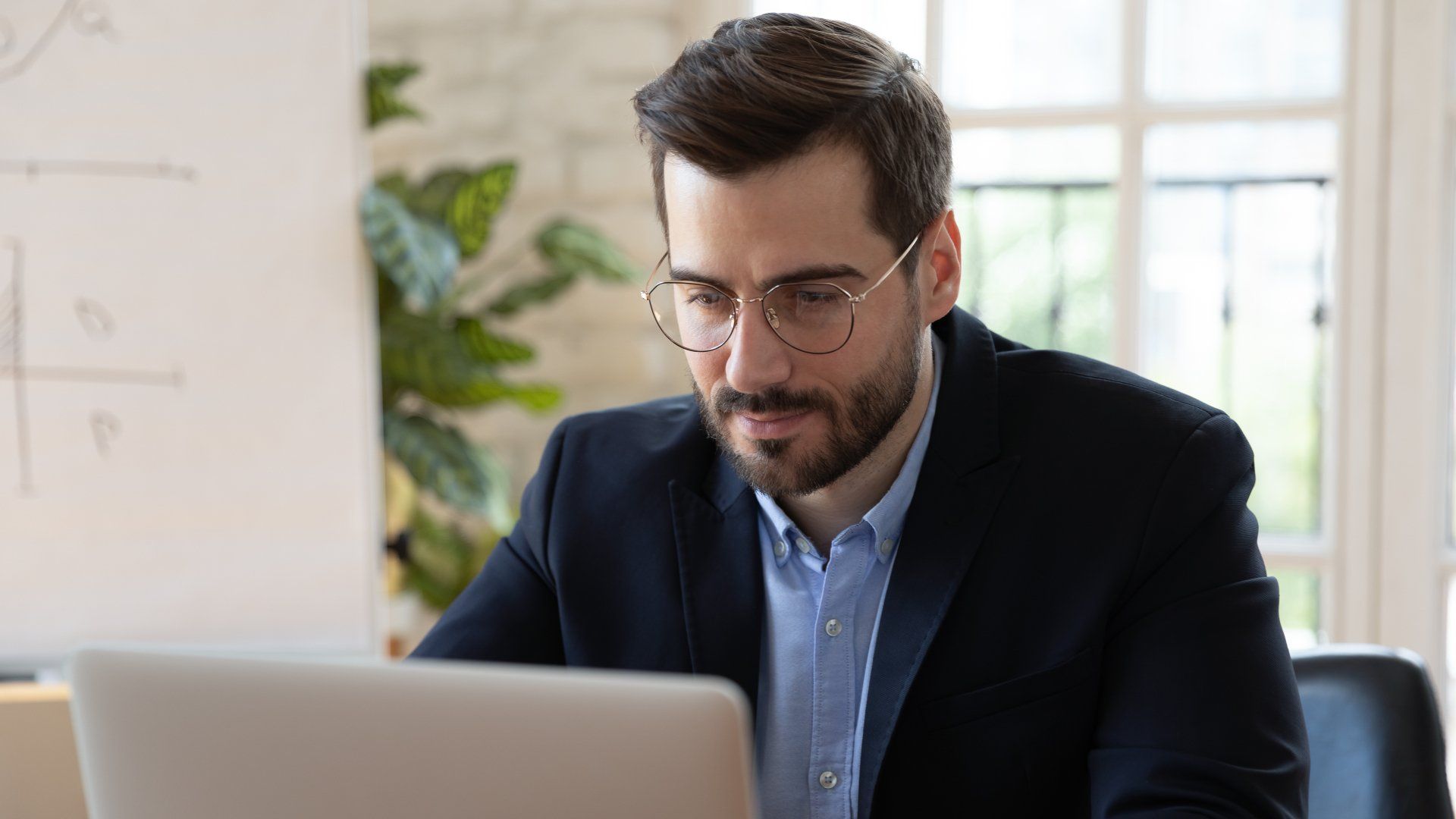 Concentrated Caucasian young male employee in glasses busy working on modern laptop