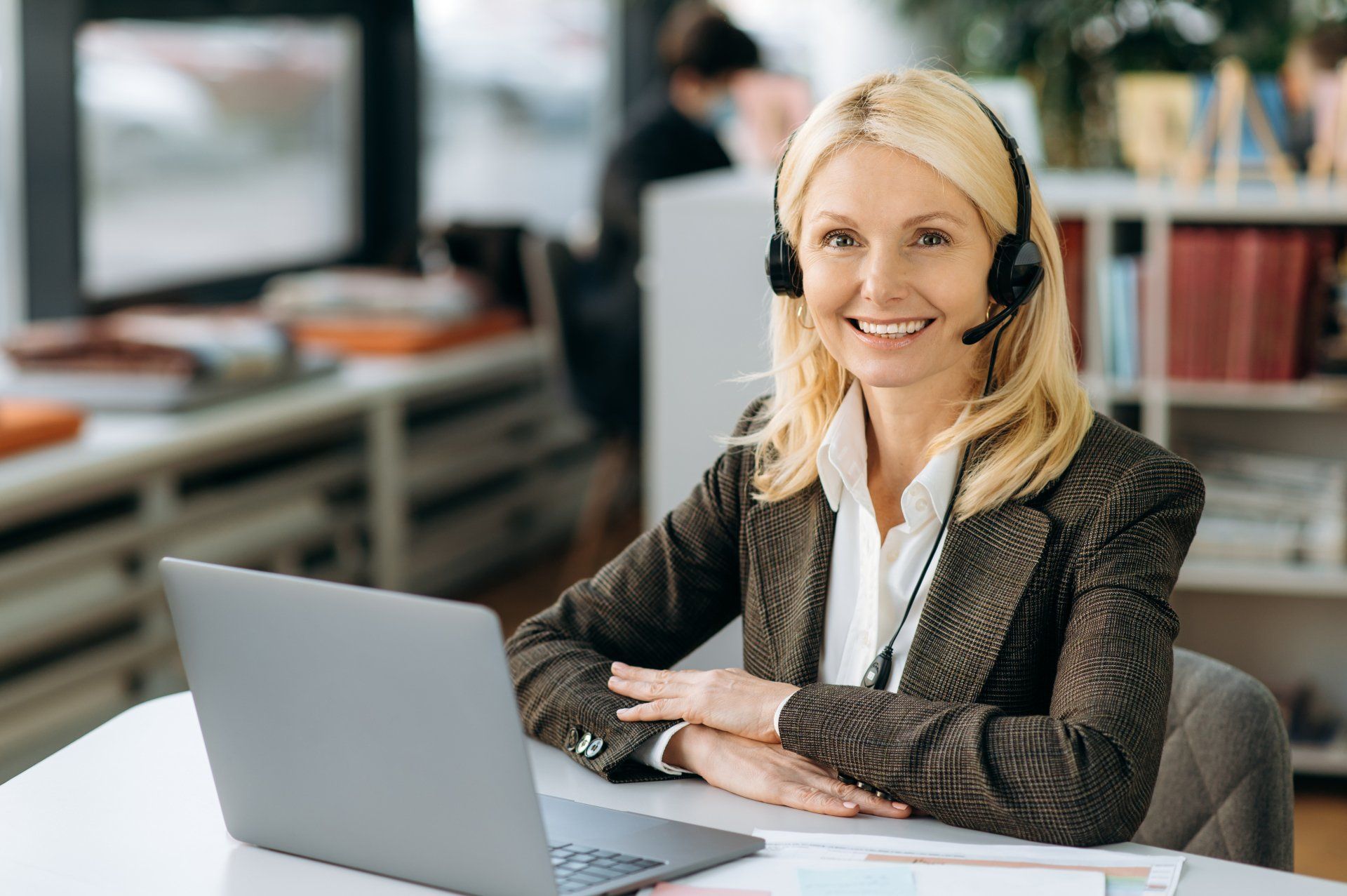 Joyful elegant female operator of call center in headset is looking at the camera, smiling