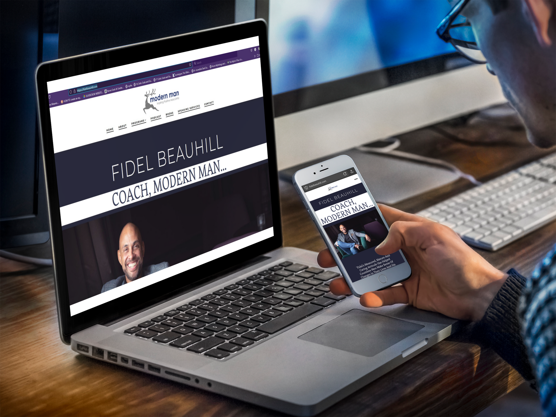 A man is holding a cell phone in front of a laptop