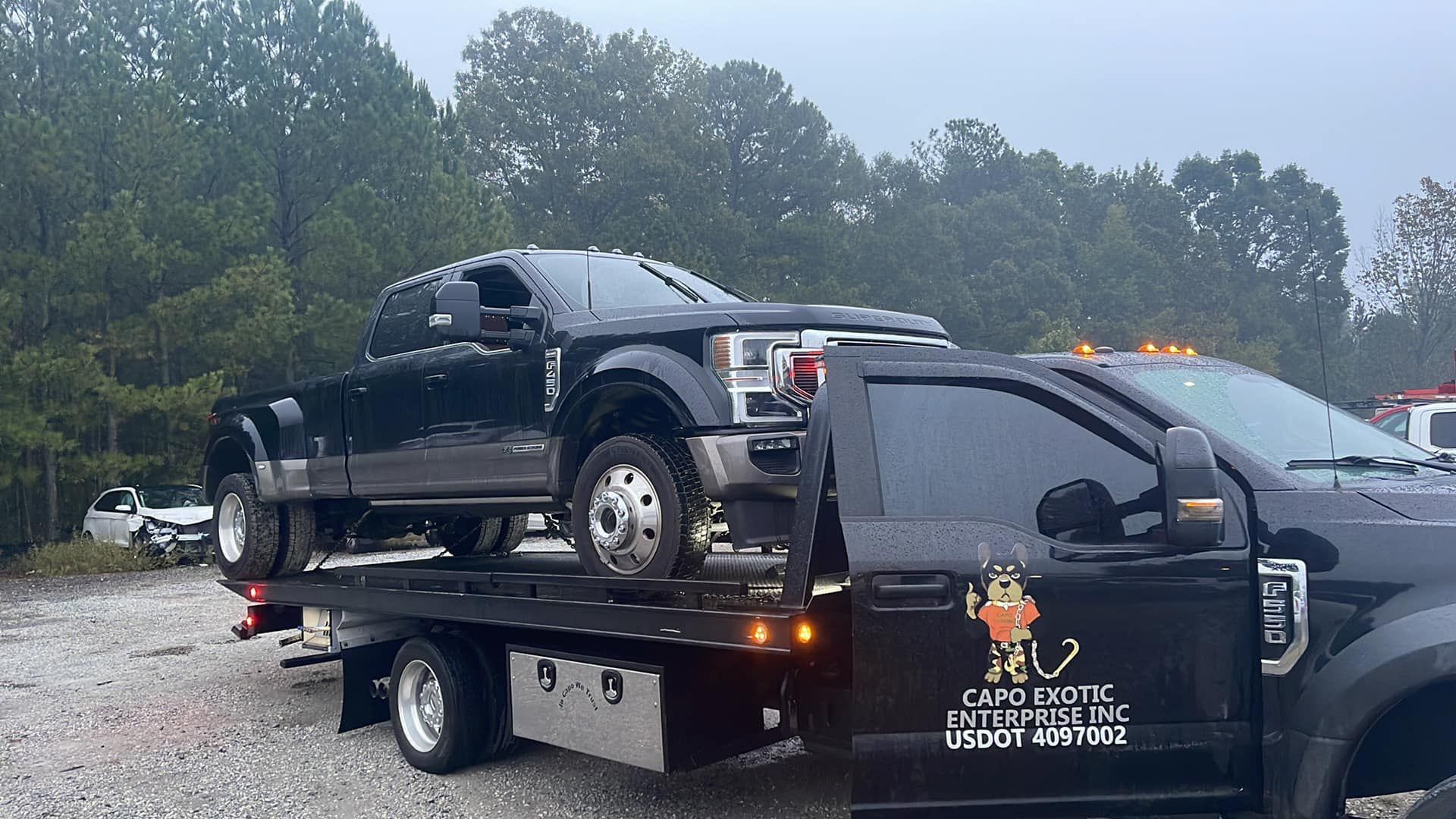 A woman is standing next to a tow truck with a car on it.