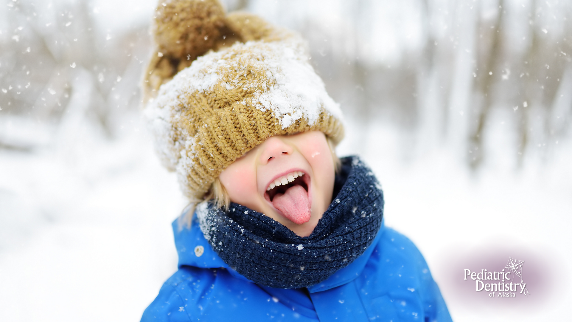 A young boy wearing a hat and scarf is sticking his tongue out in the snow