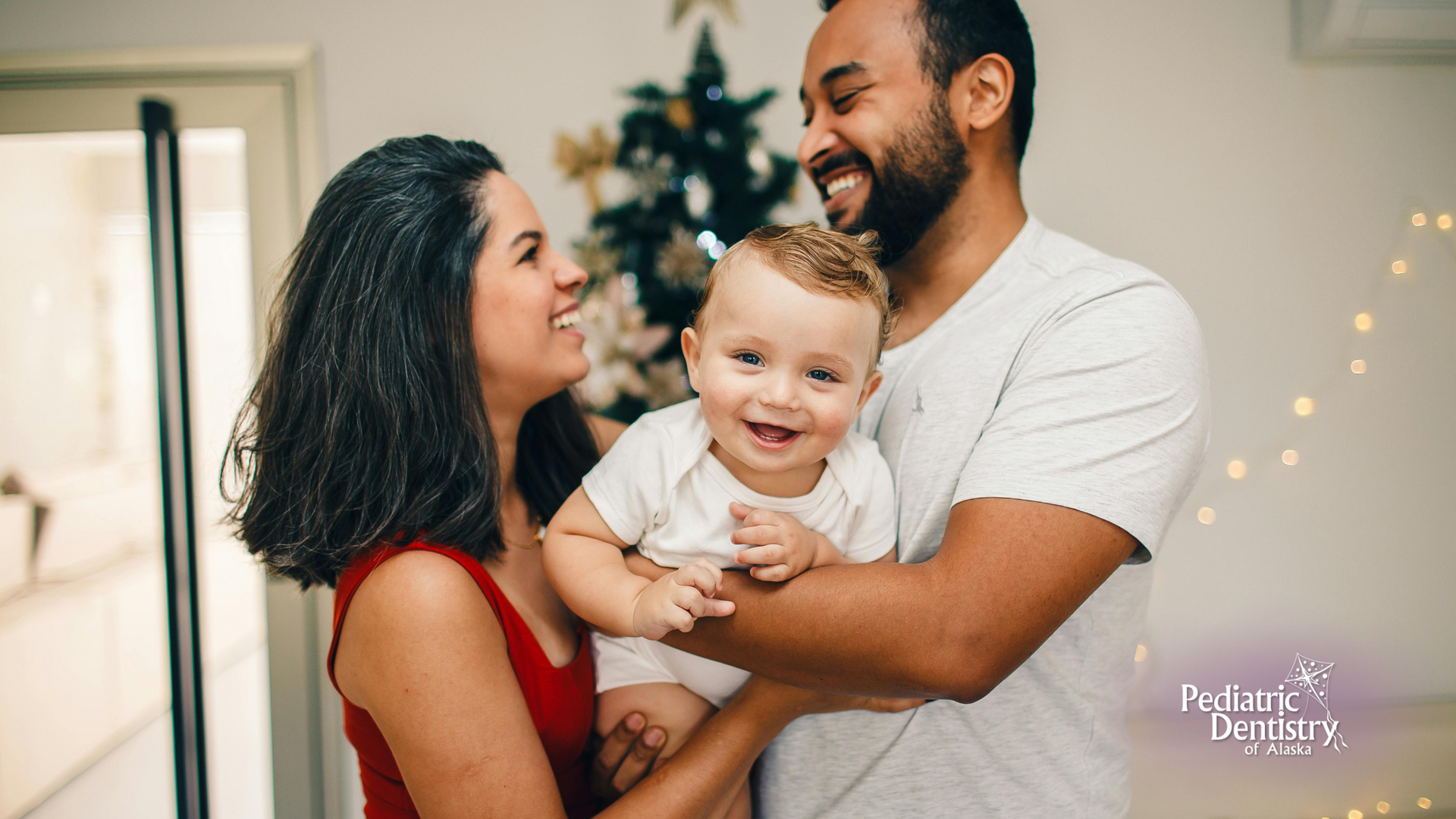 A man and woman are holding a baby in front of a christmas tree.