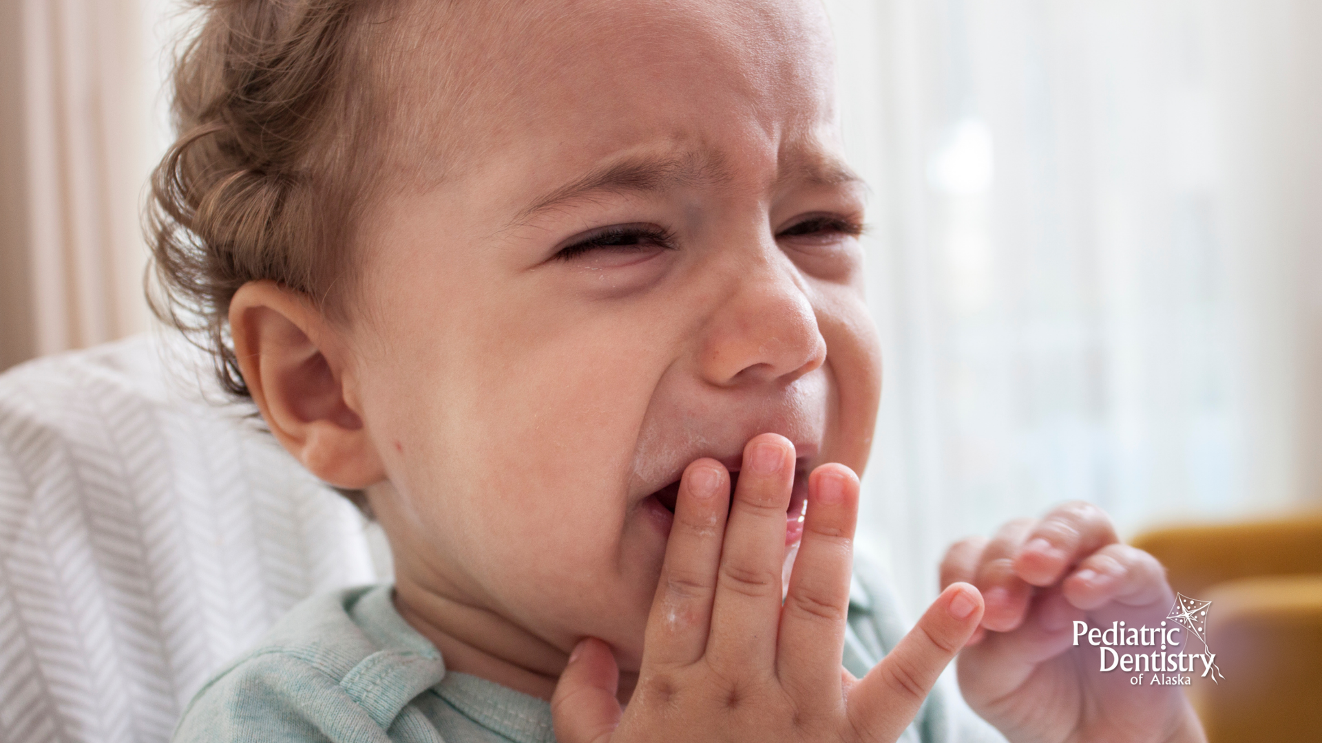 A baby is crying and covering his mouth with his hand.