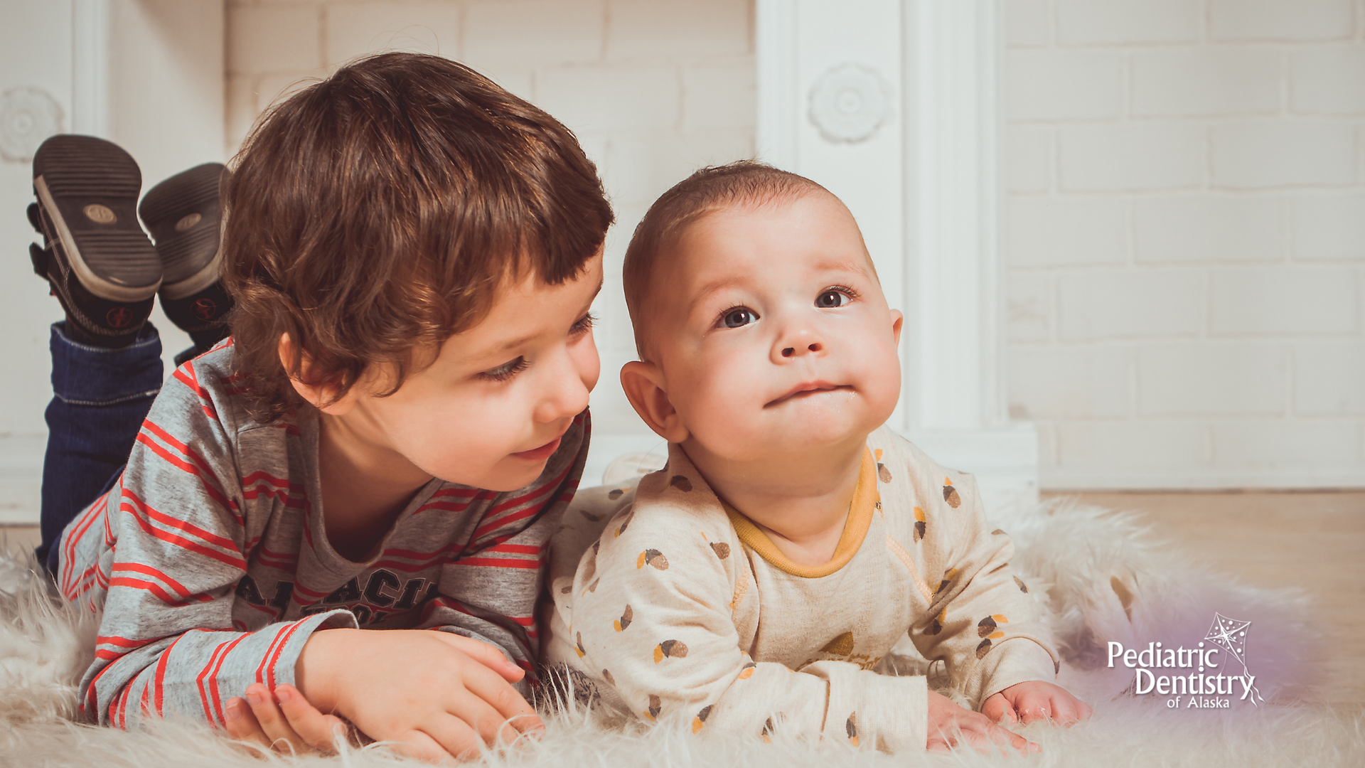 Two young boys are laying on the floor next to each other.