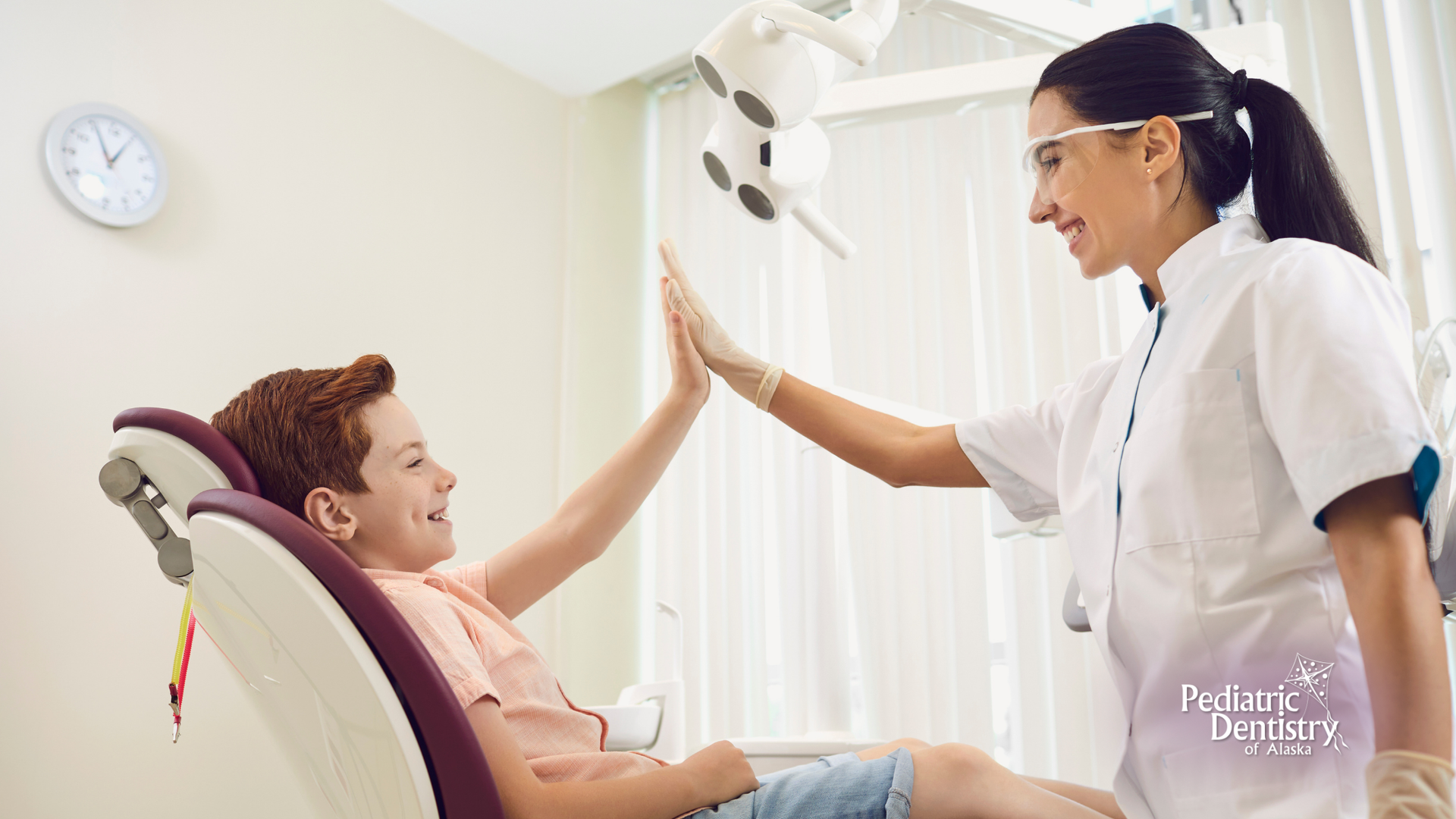 A young boy is giving a high five to a female dentist while sitting in a dental chair.