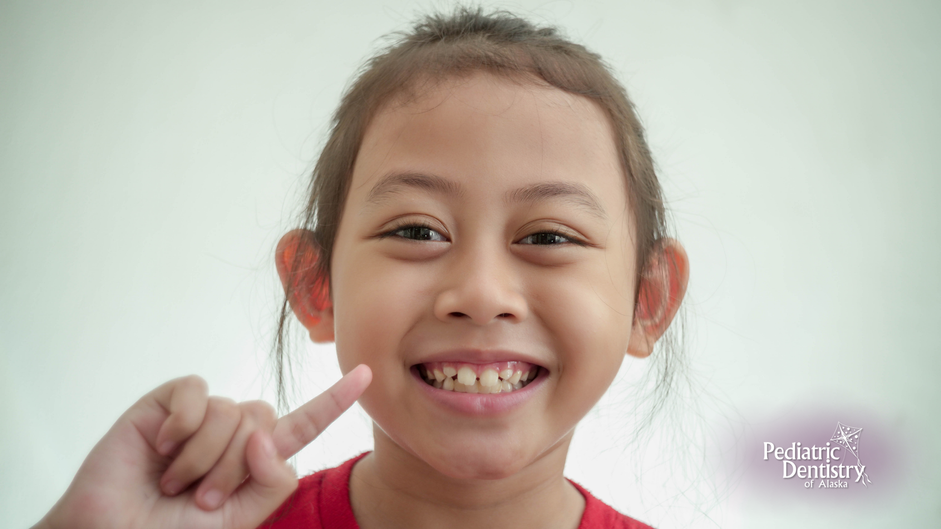 A young girl with braces on her teeth is smiling and pointing at her teeth.