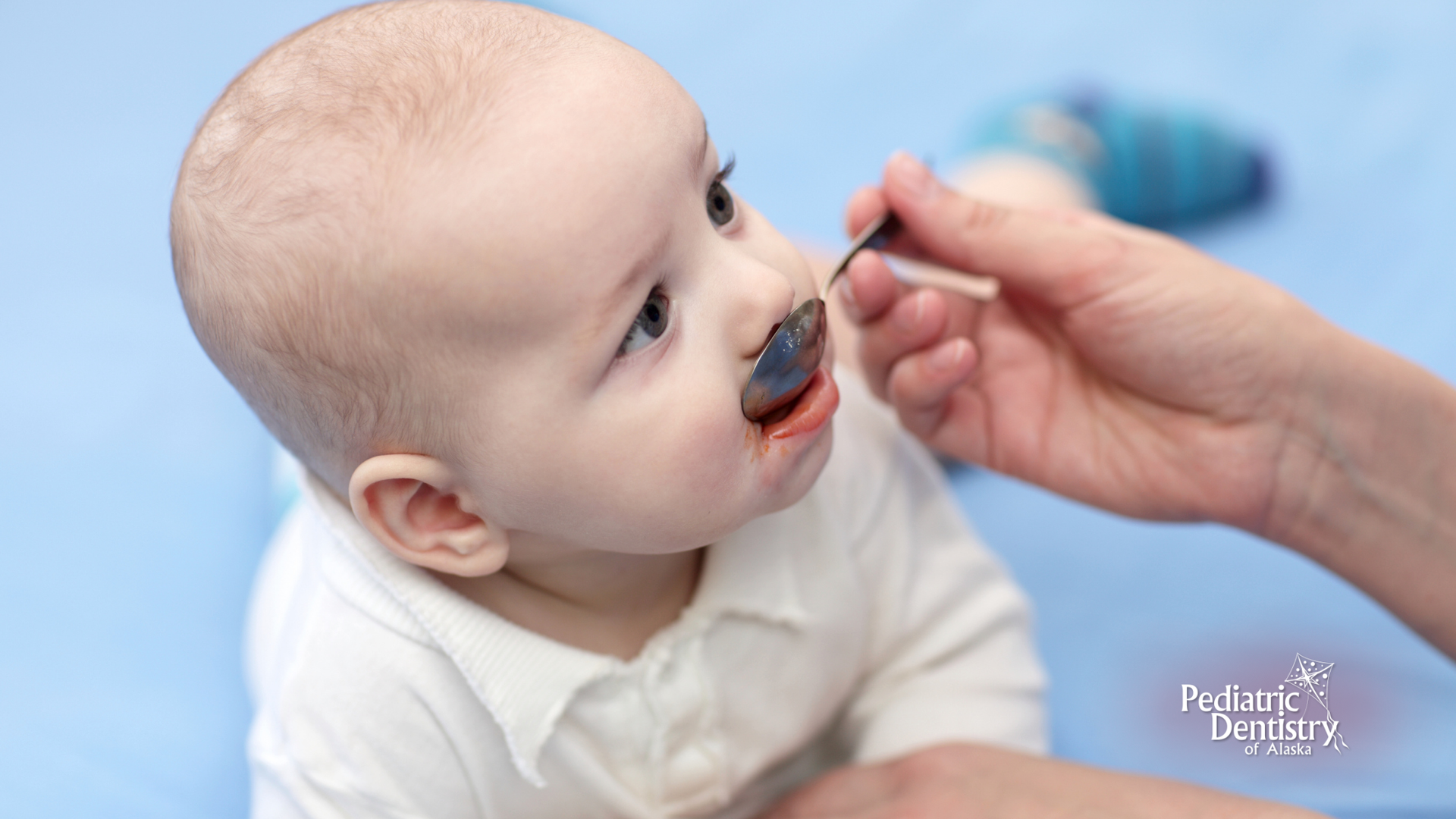 A baby is being fed with a spoon by a person.