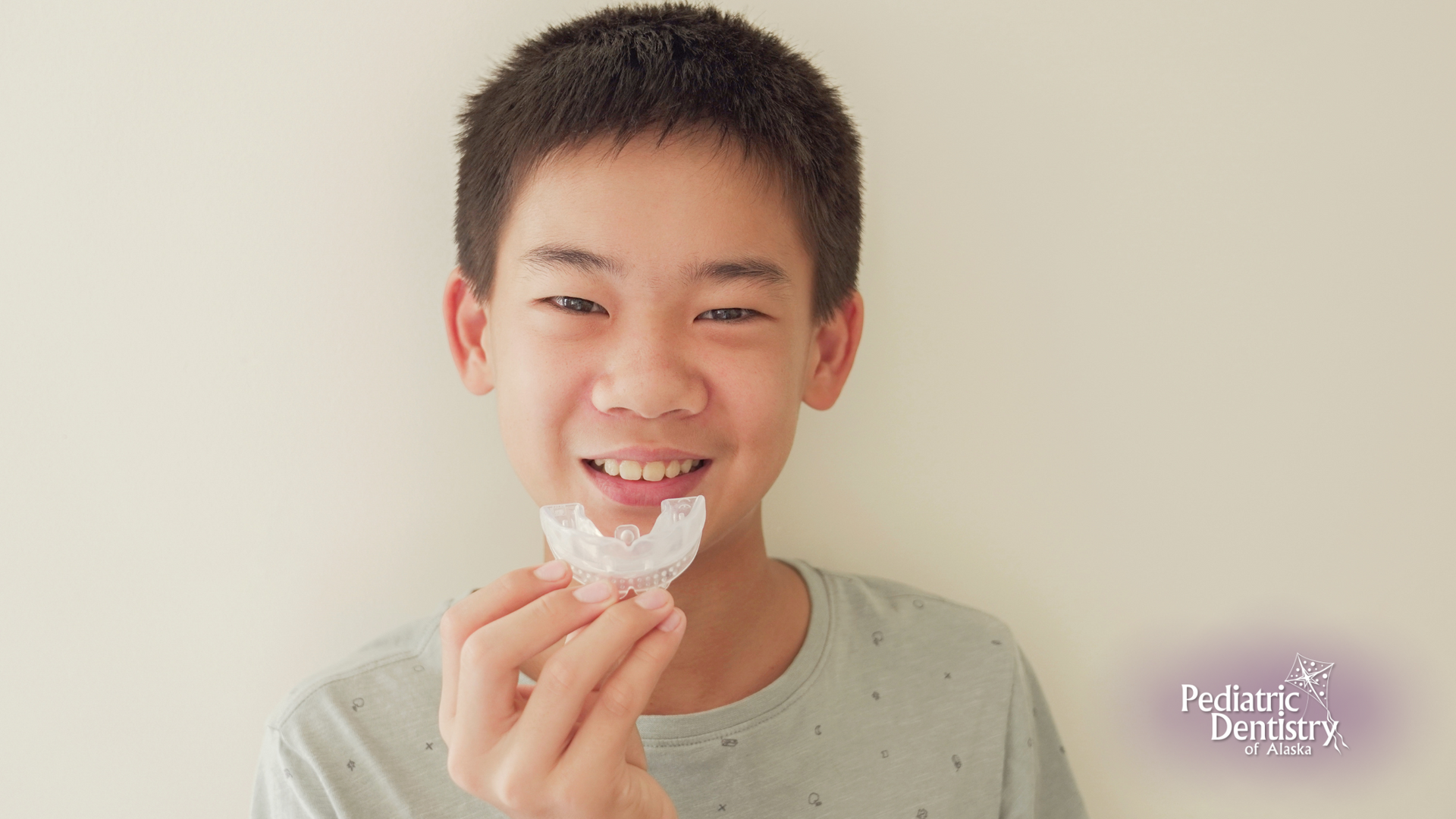 A young boy is holding a mouth guard in his hand and smiling.