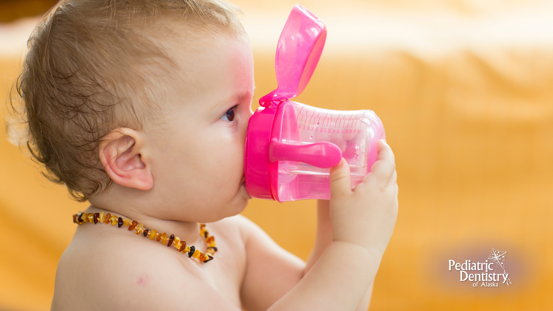 A baby is drinking water from a pink bottle.