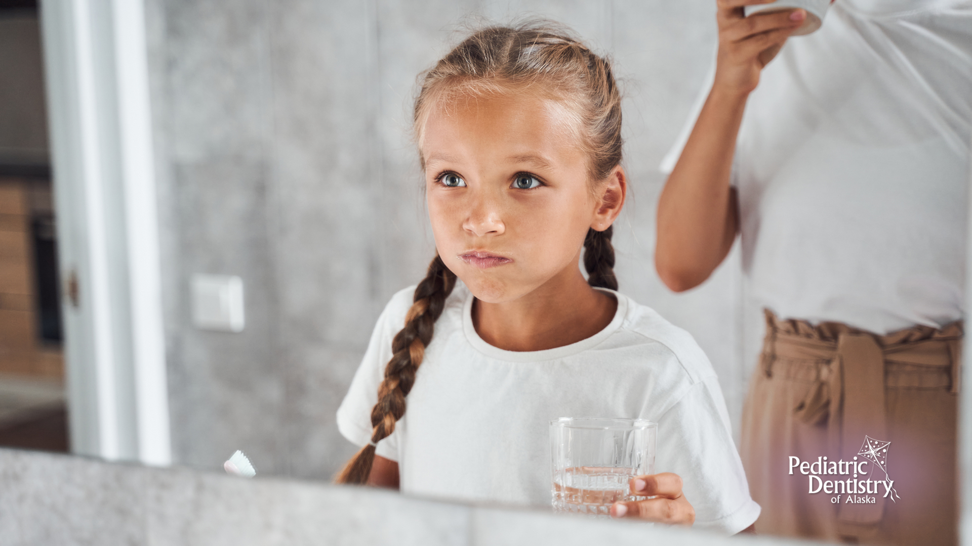 A little girl is brushing her teeth in front of a mirror.