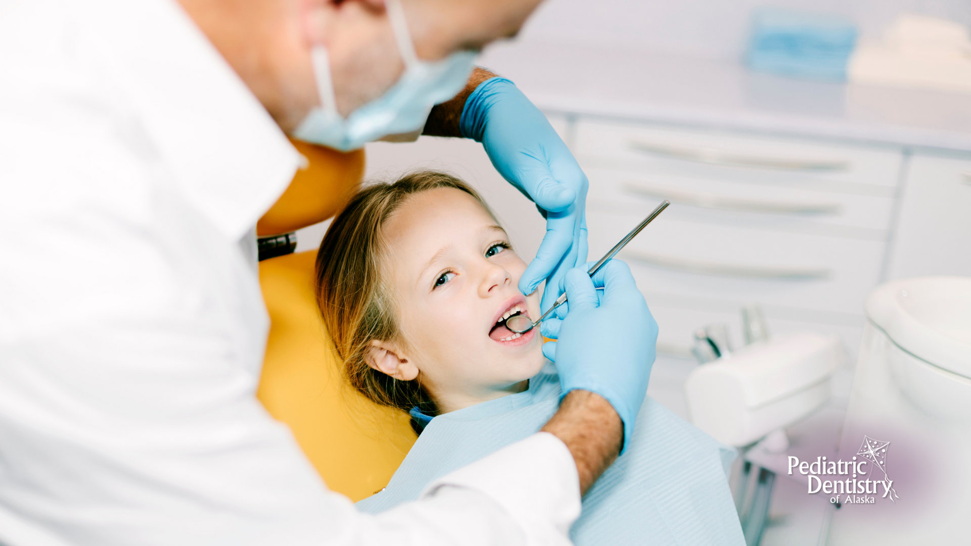 A little girl is sitting in a dental chair getting her teeth examined by a dentist.