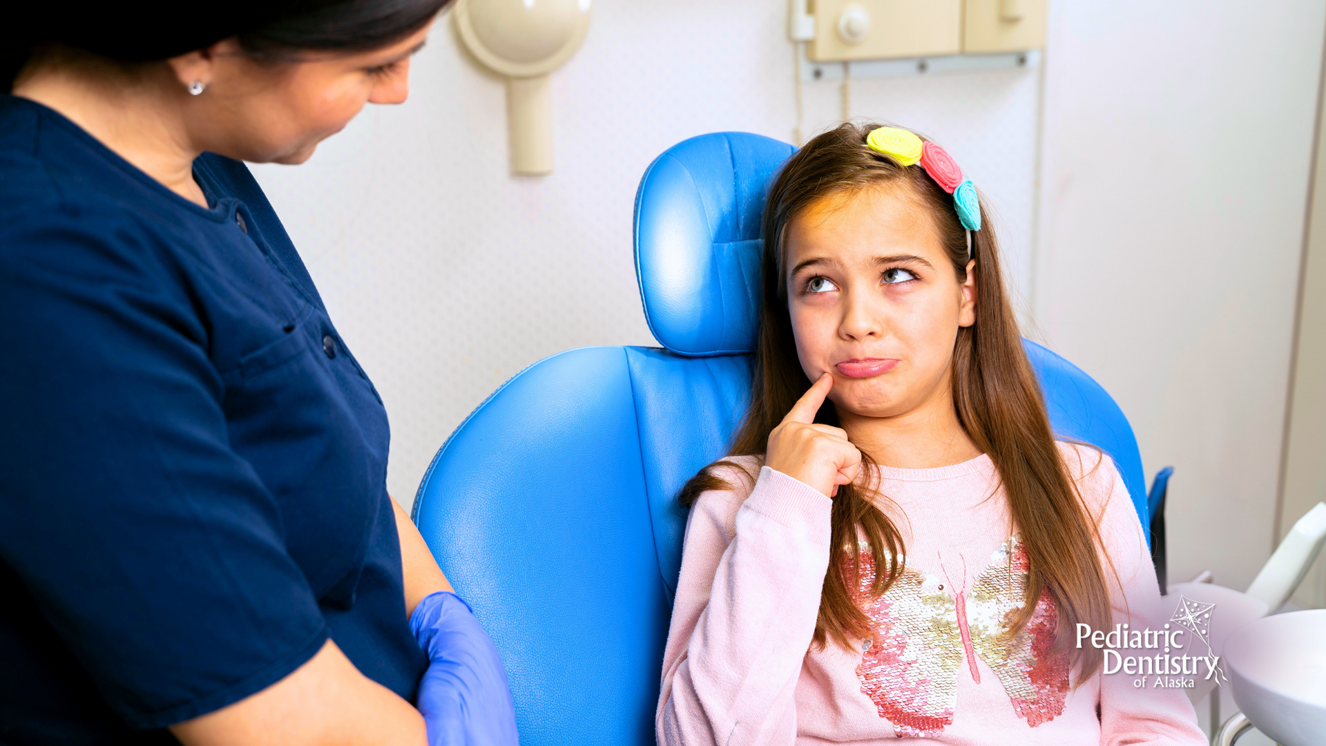 A little girl is sitting in a dental chair talking to a dentist.