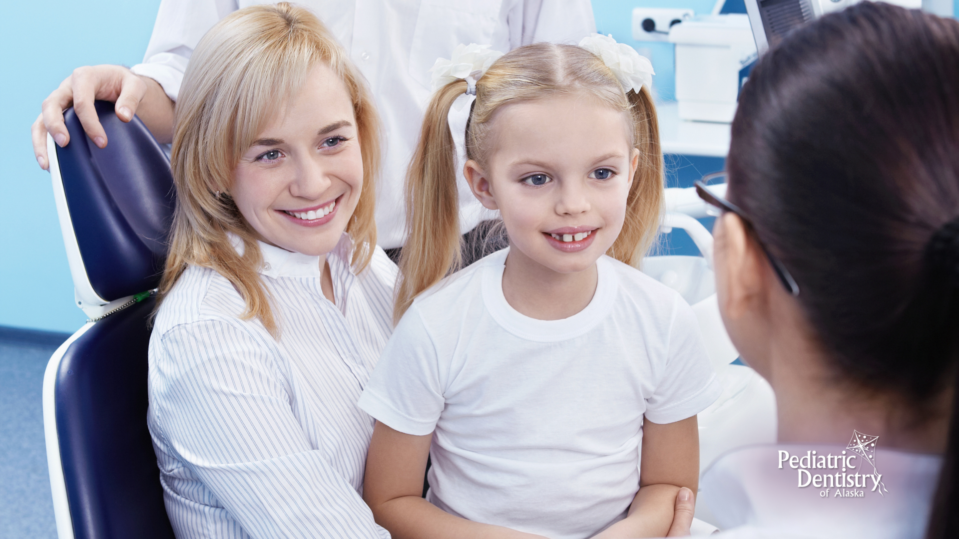 A mother and daughter are sitting in a dental chair talking to a dentist.