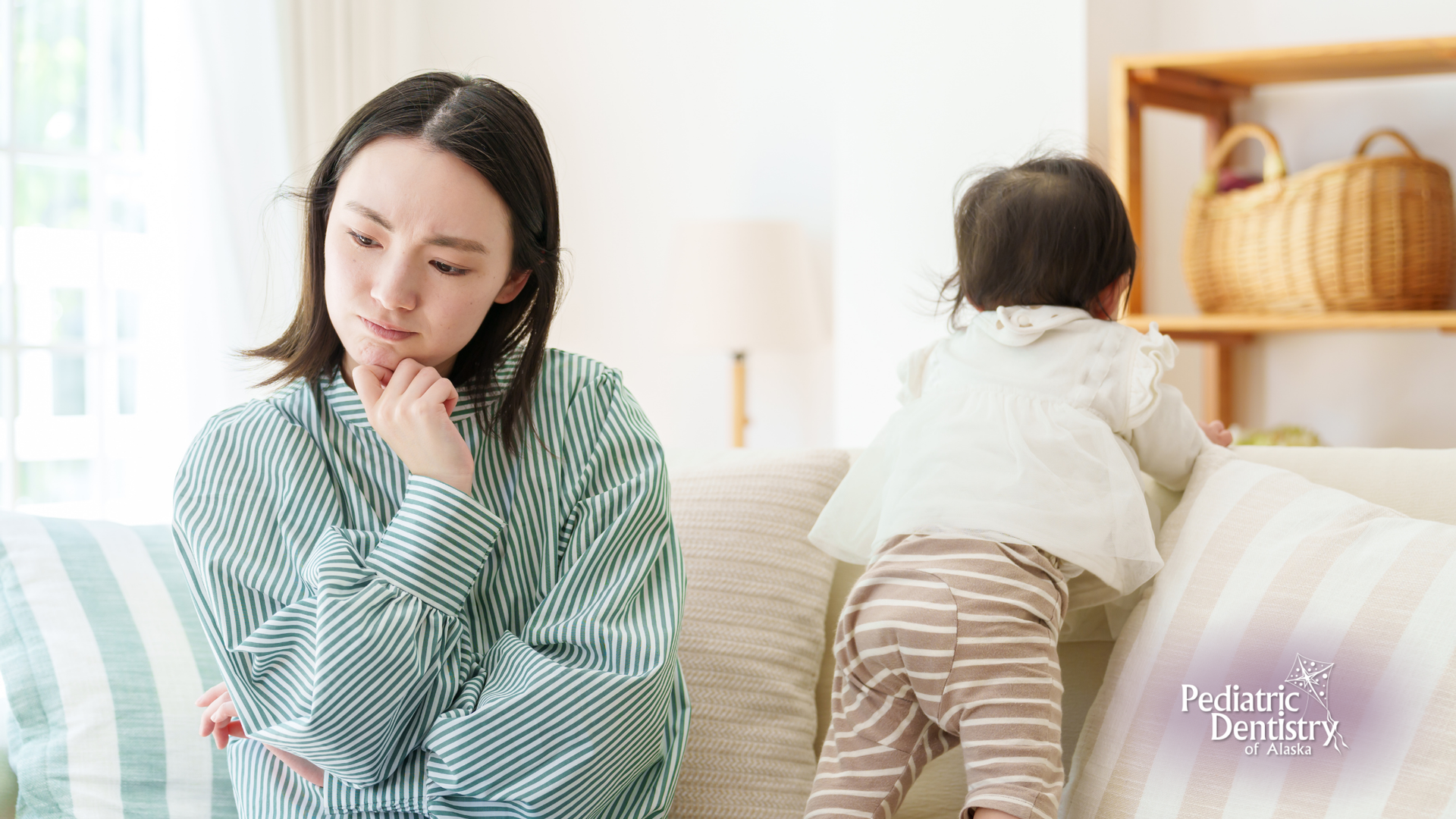 A woman is sitting on a couch with a baby in the background.