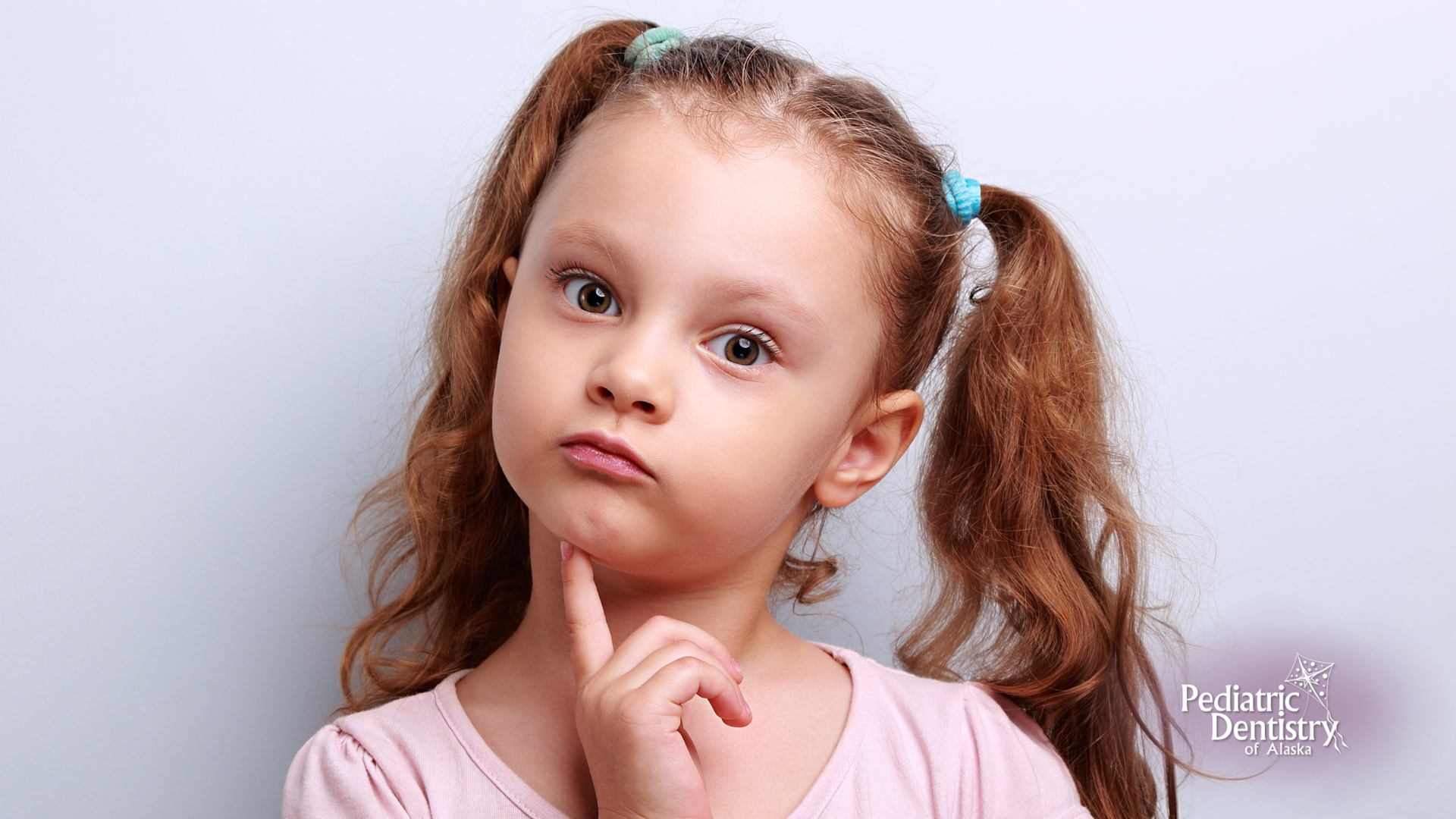 Girl with red pigtails, chin on hand, looking thoughtful against a light blue background.