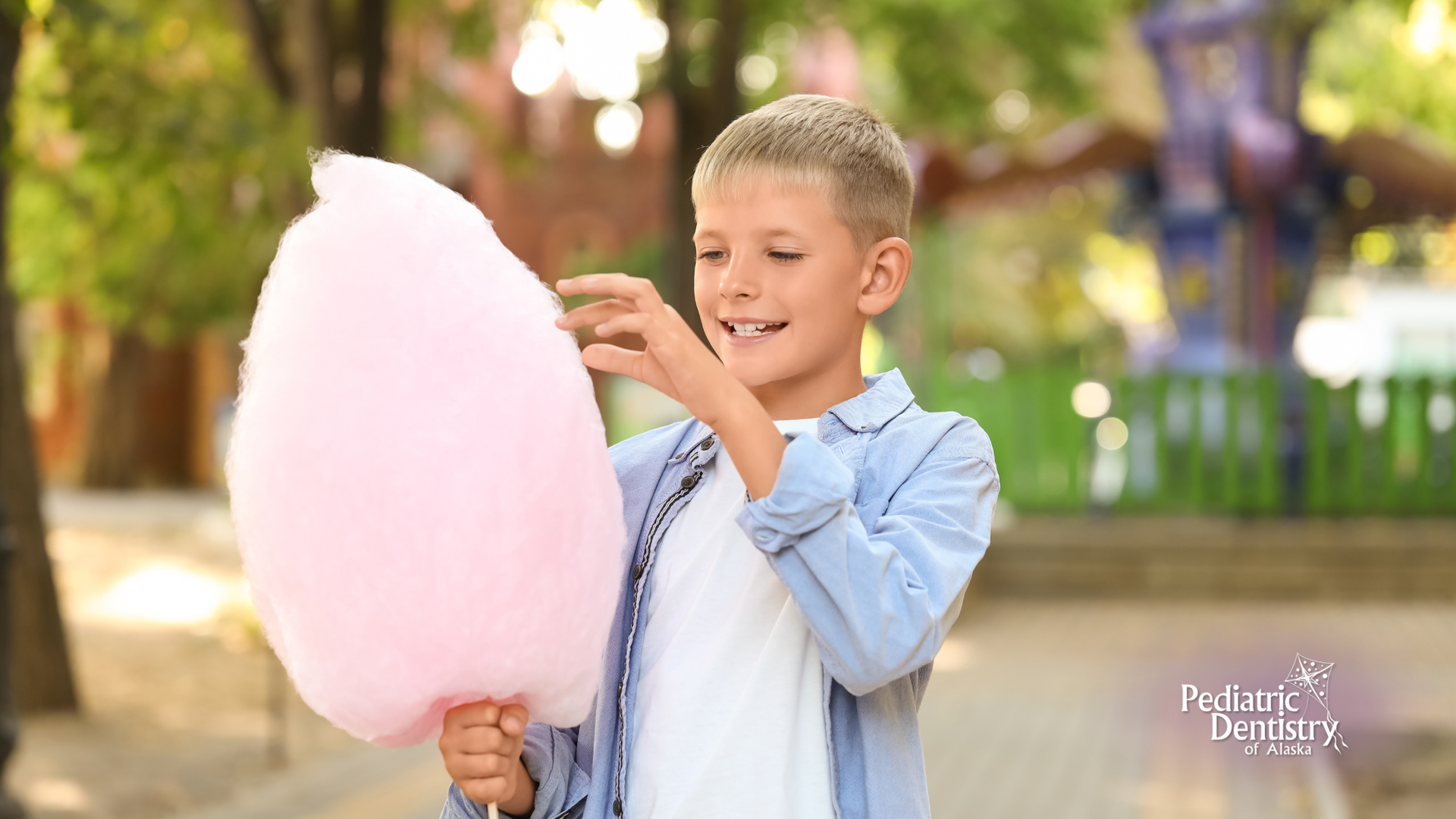 Boy holding a large pink cotton candy in a park, smiling.