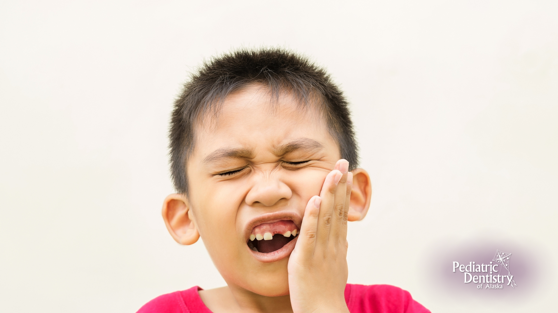 A young boy is holding his face in pain because of a toothache.