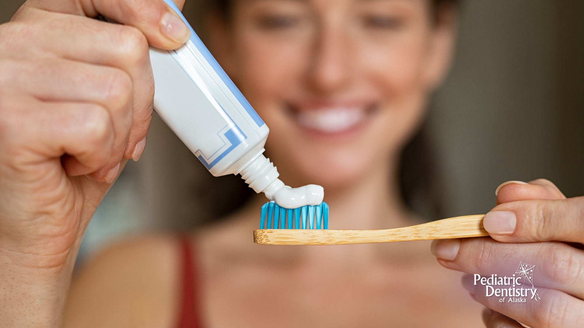 A woman is putting toothpaste on a wooden toothbrush.