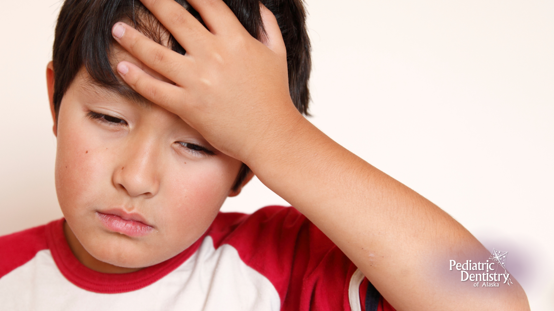 A young boy is holding his head with his hand.