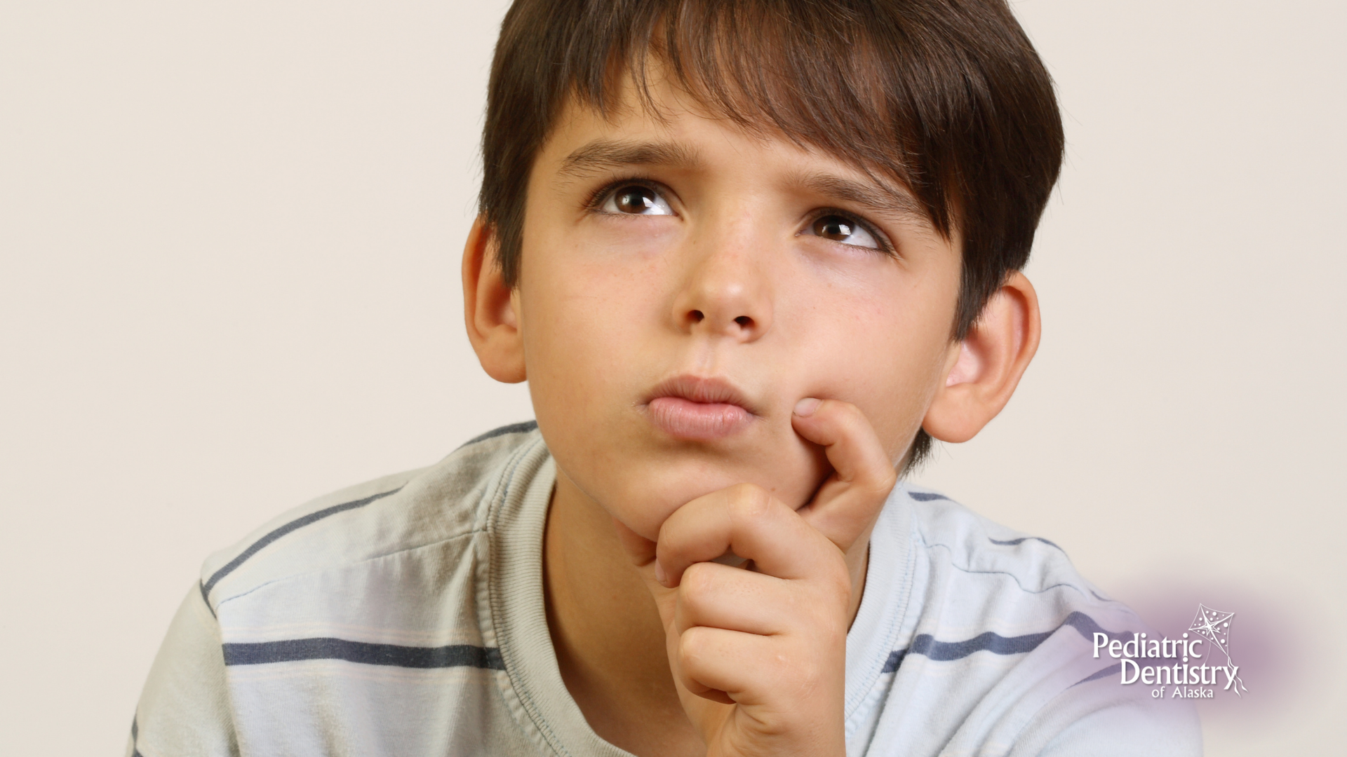 A young boy is thinking with his hand on his chin.