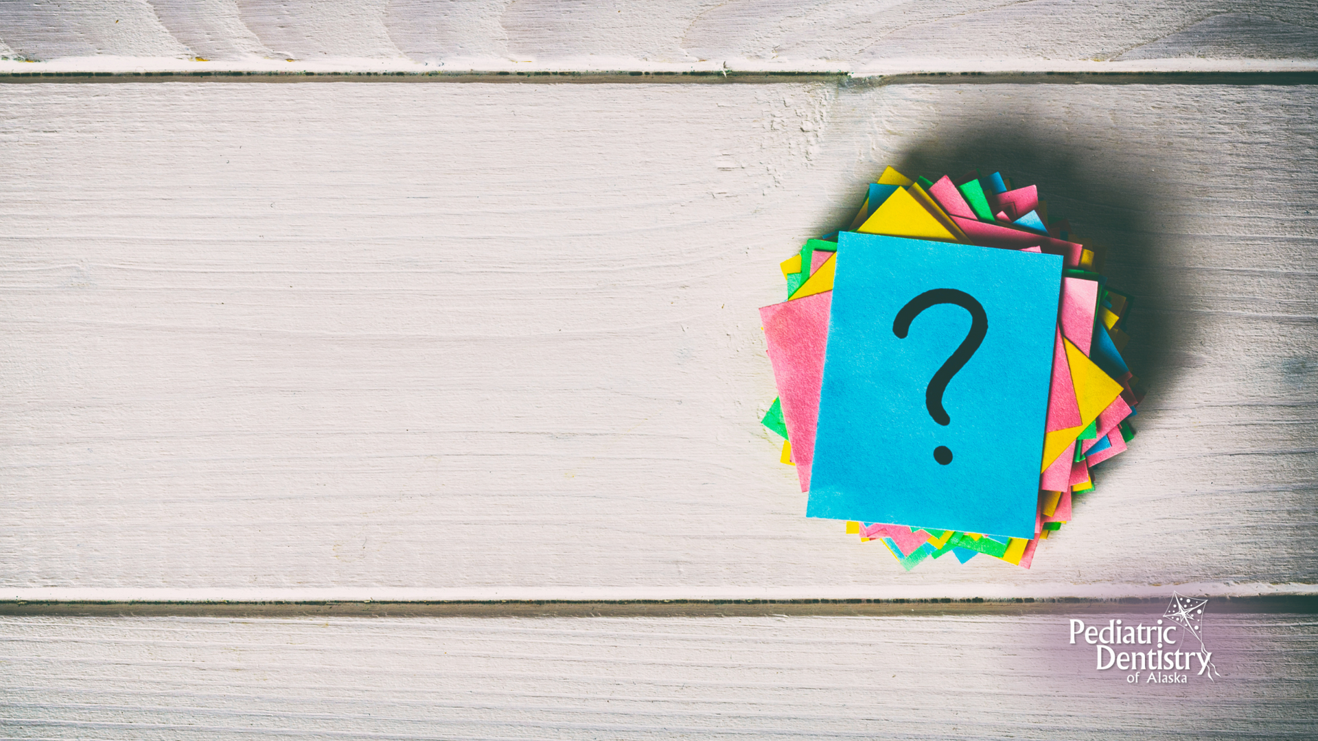 A blue sticky note with a question mark on it is on a wooden table.