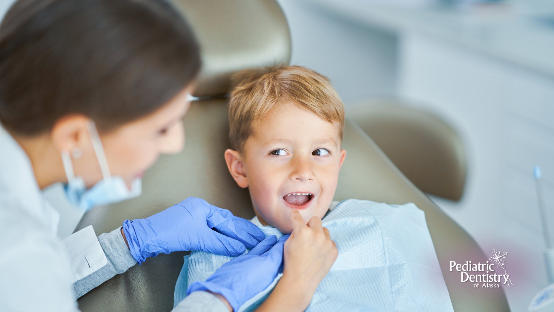 A young boy is sitting in a dental chair while a dentist examines his teeth.
