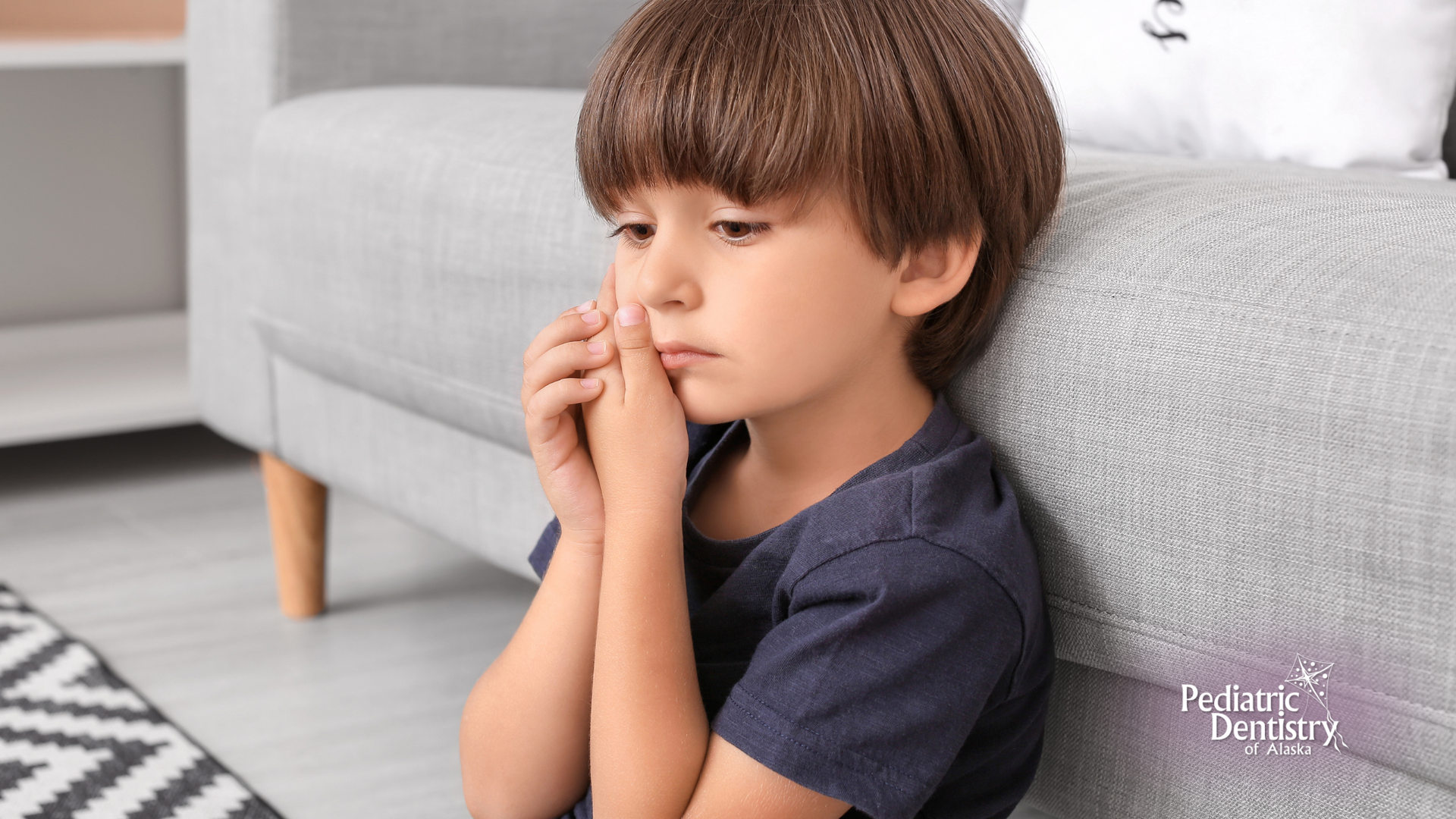 A young boy is sitting on a couch with his hands on his face.