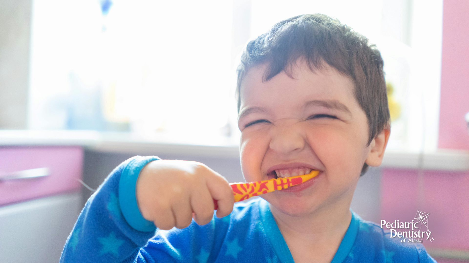 A young boy is brushing his teeth with a toothbrush and smiling.