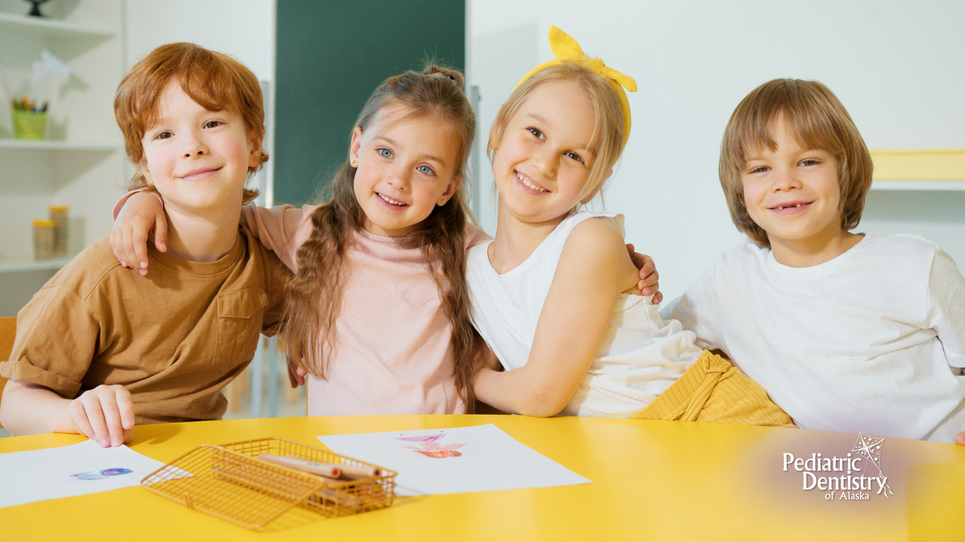 A group of children are sitting at a table with their arms around each other.